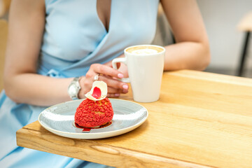 Young female drinking coffee with a piece of cake sitting at the table in a cafe outdoors