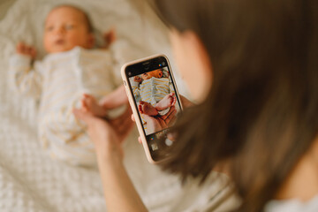 Mother taking photo of baby boy on mobile phone.