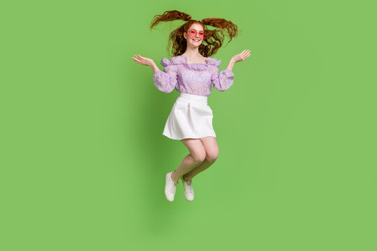 Full size photo of funny orange hairstyle millennial lady jump wear blouse spectacles skirt isolated on green color background