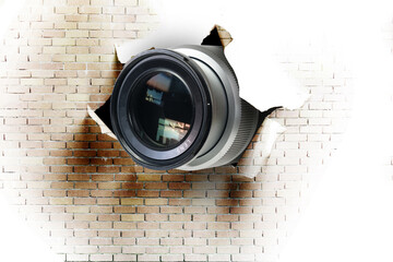 Concept of paparazzi or hidden camera, camera lens looks out through a hole in white brick wall