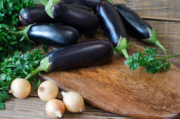 Whole raw eggplant, onions and parsley on wooden cutting board.