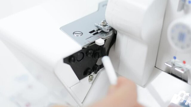 Cleaning the overlock sewing machine. Women's hands hold a small brush for cleaning debris, remnants of fabric.