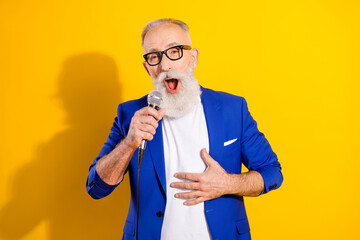 Photo of happy cheerful old man sing hold hand mic karaoke wear glasses isolated on yellow color...