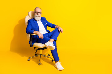 Full size photo of focused aged man sit in leather chair look attentively camera isolated on yellow color background