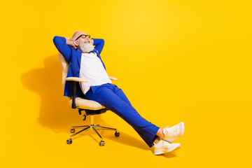 Full length body size view of attractive elegant cheerful man sitting in office chair resting isolated over bright yellow color background