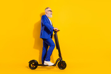 Full body profile photo of grey beard old man ride scooter wear spectacles blue suit isolated on yellow background