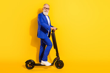 Full size photo of happy smiling good mood mature businessman riding eco scooter isolated on yellow color background