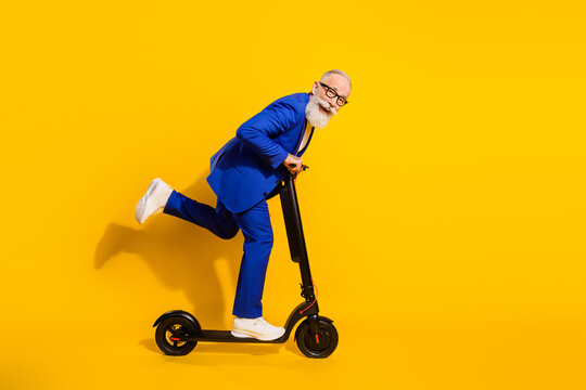 Full size profile side photo of happy smiling good mood mature man riding eco scooter isolated on yellow color background