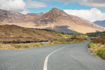 Small narrow asphalt road in Connemara, county Galway, Ireland. With beautiful nature view. Irish landscape. Cloudy sky. Warm sunny day. Travel concept