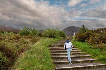 Teenager girl walking on a stair way to Croagh Patrick, county Mayo, Ireland. Cloudy sky. Mountain...