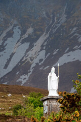 White statue of Saint Patrick holding green shamrock at the start of foot path to the peak of...