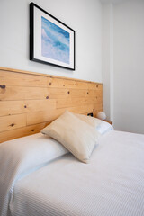 Bright white bedroom interior decorated with a photo of sea waves and a wooden headboard