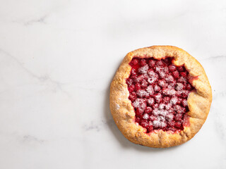 Perfect raspberry galette. Delicious rustic homemade tart with frozen or fresh raspberries on white marble background. Beautiful round shape galette with raspberries,copy space. Top view or flat lay