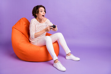 Photo of funny sweet woman wear knitted shirt sitting beanbag playstation looking empty space isolated violet color background