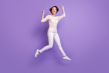 Full length photo of excited lucky young lady dressed white shirt rising fists jumping isolated purple color background