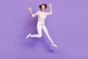Fototapeta na wymiar Full size photo of cheerful pretty lady jumping have fun raise hands isolated on violet color background