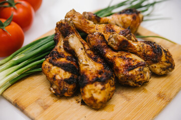 Fried chicken legs lie on a wooden board. Chicken shish kebab with a side dish of vegetables and green onions.