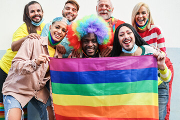 Gay people smiling at pride parade with LGBT flags while wearing protective face mask - Main focus...