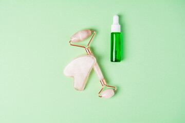 Roller and gua sha massage scraper and beauty product on a green background. Serum or oil and skincare tools. Wellness concept. Copy space