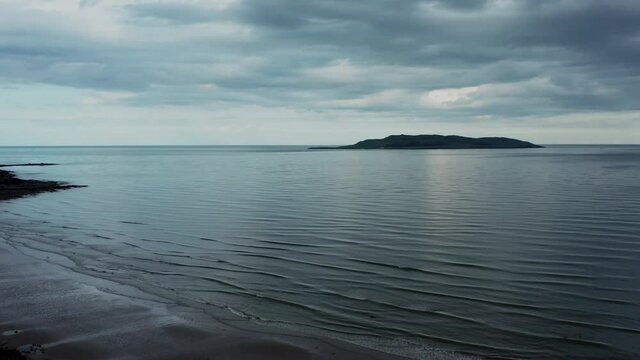 Cinematic aerial view over beach landscape and revealing the Irish sea and Lambay Island on a cloudy evening  Donabate beach in summer, Dublin, Ireland