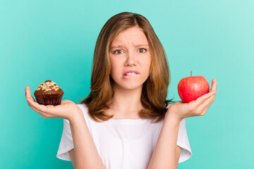 Photo portrait girl scaling sweet cupcake apple biting lip sad keeping diet isolated vivid teal...
