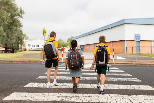 Three public school kids walking to school - crossing the road at a pedestrian crossing