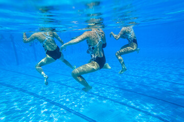 Synchronized Swimming Girls Team Unrecognizable Dance Underwater photography closeup action in blue pool water. 