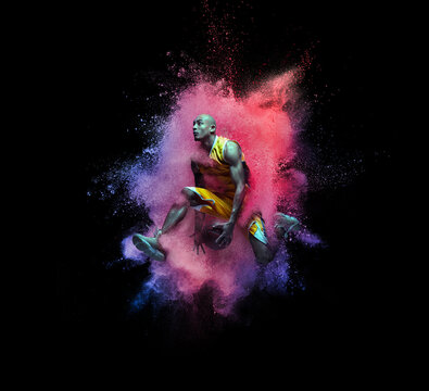 One young sportsman basketball player in explosion of colored neon powder isolated on black background