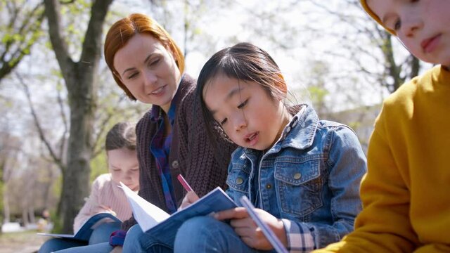 Teacher with small children sitting outdoors in city park, learning group education and coronavirus concept.