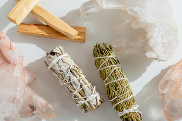 White sage, cedar, crystals, and Palo Santo sticks tied by a bundle on a light background. A set of...