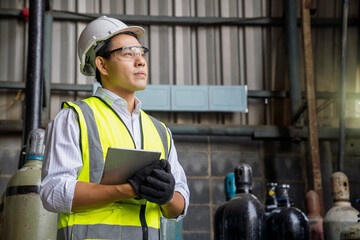 Industrial worker holding tablet in manufacturing gas. Acetylene and oxygen gas steel storage tanks...
