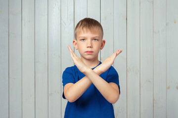 serious preteen boy in blue t shirt holding two arms crossed, say no, stop gesture, warning of end...