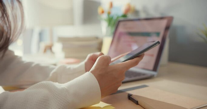 Close-up young asia lady freelance focus mobile phone chat with colleagues work finance graph account chart market plan in laptop at home. Girl student learn online at house, Work from home concept.