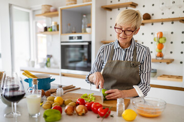 Beautiful mature woman in apron is preparing food and smiling while cooking in kitchen