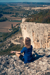 Fototapeta na wymiar Young woman sits on a rock, looking at the landscape and enjoying the view and fresh air.