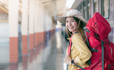 Obraz premium Beautiful asian traveler with backpack smiling and looking at camera while while preparing to travel at railway station.