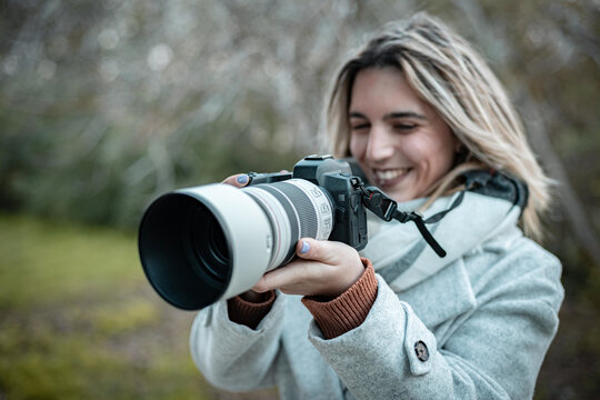 Smiling woman taking photos on professional camera in nature