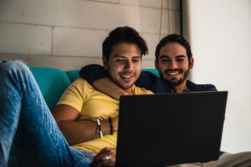 Ethnic gays sharing laptop while resting on couch at home