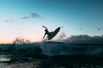 Unrecognizable athlete practicing surfing on ocean wave at sunset