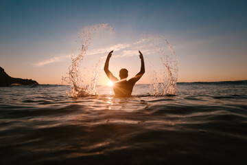 Unrecognizable sportsman in sea with splattering water in sunshine