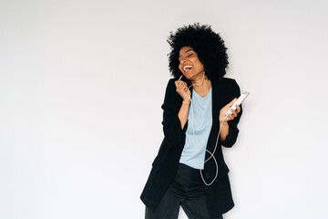 Happy black woman dancing and singing while listening to music on smartphone