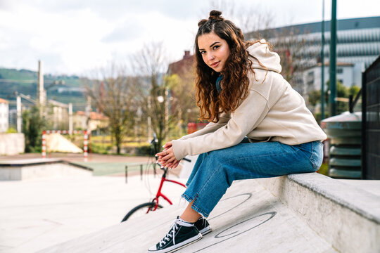 Woman with buns on head resting on parapet near bicycle