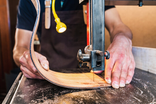 Anonymous luthier cutting guitar body on bandsaw in workroom