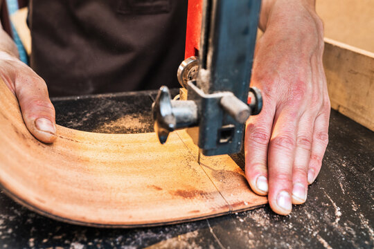 Anonymous luthier cutting guitar body on bandsaw in workroom