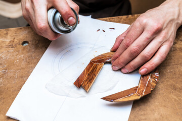 Crop luthier spraying wooden piece in workshop