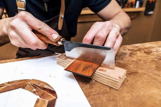 Crop craftsman cutting wooden piece with saw in workshop