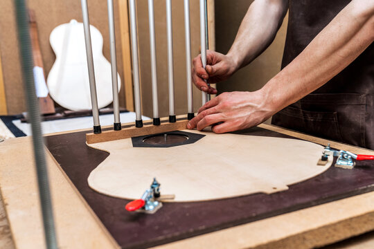 Craftsman installing metal sticks while building guitar in workroom