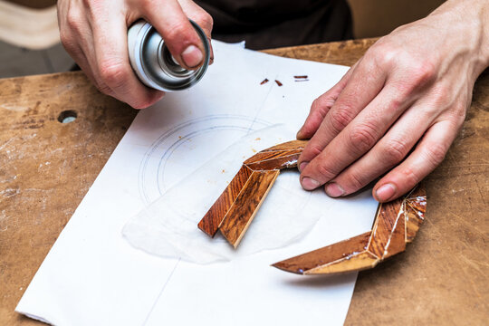 Crop luthier spraying wooden piece in workshop