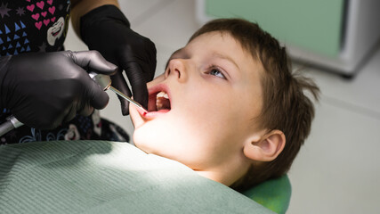 Boy's face in dental chair and hands of dentist in gloves with tool