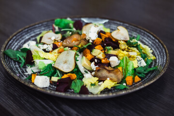 Clay plate with vegetable salad of caramelized pear, beetroot, arugula, avocado, carrot, with dorblu cheese